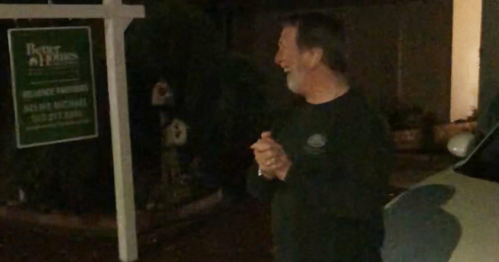 Craig Cooper watches a parade of cars pass his house.