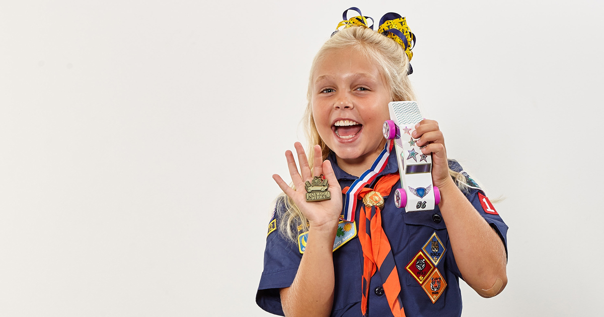 Female Cub Scout holds Pinewood Derby car and medal