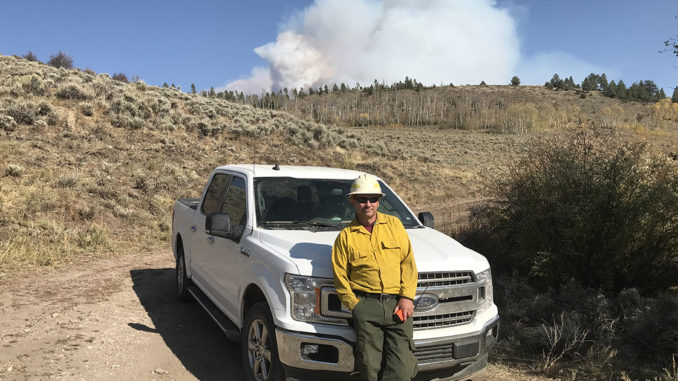 Mike Huneke stands with a truck with smoke in the distance.