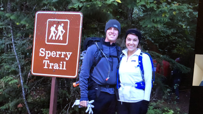 A couple smiles in front of a trailhead.