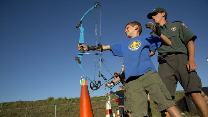 Scout camp staffer helps camper with archery at summer camp