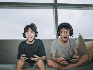 sibling brother sitting on sofa playing online video games with headset in living room during weekend