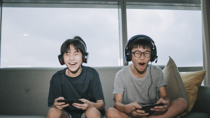 sibling brother sitting on sofa playing online video games with headset in living room during weekend