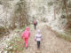 A photo of a parent and two children walking along a trail in the snow