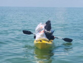 A photo of a kayaker carrying a bag of trash to shore