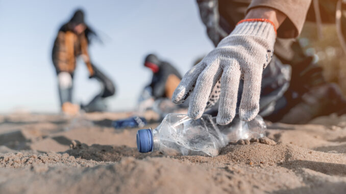 A photo of a person picking up trash from a beach