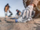 A photo of a person picking up trash from a beach
