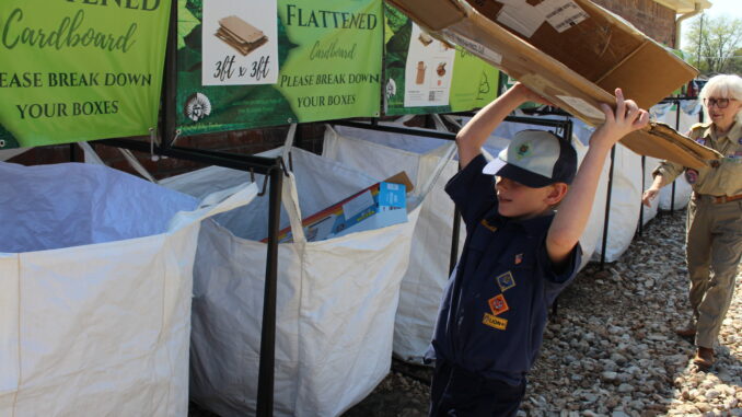 A Cub Scout drops off a piece of cardboard into a recycling bin operated by the Cherokee Area Council