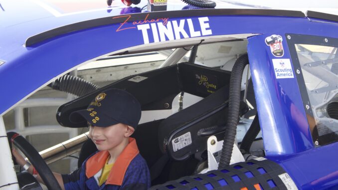 A photo of Cub Scout James Bryan sitting behind the wheel of a real race car