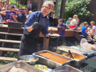 A photo of an Upper Crust Food Service chef preparing a meal for a group of campers