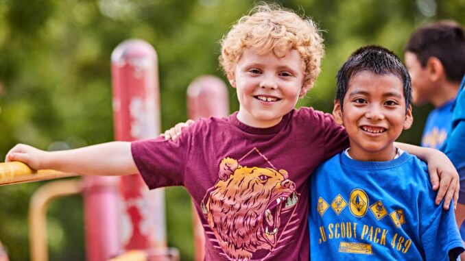 Adventure On 2023 Social Media Image - #AdventureOn - Two cub scouts with arms around each other at the playground; jungle gym; friends; pals